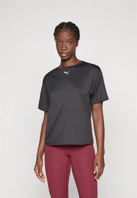 T-shirt de sport noir à manches courtes en tissu lisse et léger, arborant un logo Puma blanc sur la poitrine. Associé à des leggings moulants bordeaux.