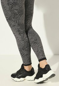 Leggings en imprimé animal noir et gris avec une texture lisse ; assortis à des baskets noires avec des semelles blanches épaisses et des accents texturés.