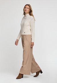 Krämfärgad kabelstickad polotröja kombinerad med beige vida byxor och bruna ankelboots med klack. Mjuk textur och åtsittande silhuett.