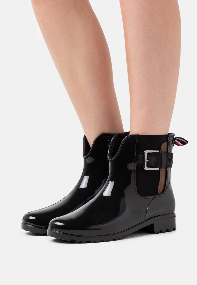 Bottines noires en cuir verni avec un bout rond, des panneaux latéraux élastiques et une boucle décorative sur le côté extérieur, dotées d'une semelle texturée.