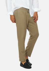 Pantaloni in lino beige con vita con cordoncino, caratterizzati da pieghe e gambe affusolate, abbinati a mocassini neri.