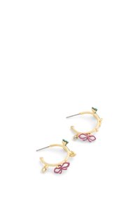 Boucles d'oreilles en or en forme de créole ornées d'un accent en forme de nœud rose, de détails verts et d'un petit charme en pierre précieuse. Elles ont une surface lisse et une forme circulaire.