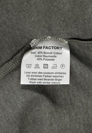 Grijze stoffen label met verzorgingsinstructies en samenstelling van de stof: 60% katoen, 40% polyester, met symbolen voor wassen en drogen.