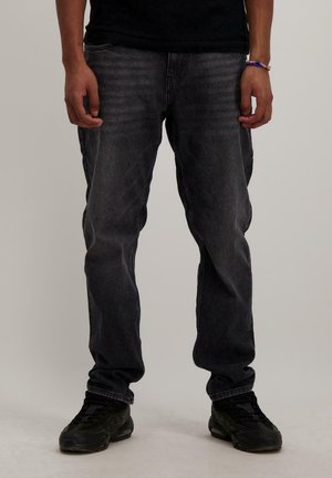Zwarte denim jeans met een rechte pijpstijl, voorzien van een versleten wasmachine en minimale stikseldetails. Draagt zwarte sportschoenen.