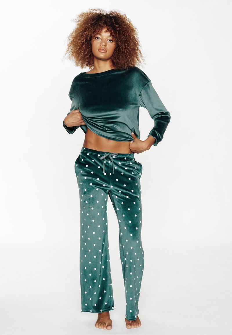 Ensemble de loungewear en velours de couleur vert profond. Haut à manches longues avec une coupe décontractée. Le pantalon est orné de pois blancs et possède un cordon de serrage à la taille. Texture lisse.