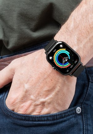 Montre intelligente noire avec un écran rectangulaire affichant des graphiques circulaires colorés, portée au poignet d'une peau claire, au-dessus d'une poche en denim foncé.