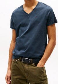 Navy blue v-neck t-shirt made of cotton, featuring short sleeves and a small logo on the chest, paired with olive green cargo pants.