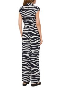 Combinaison avec imprimé zèbre en noir et blanc, dotée d'un col, de manches courtes, et de pantalons à jambes larges, fabriquée dans un tissu texturé.