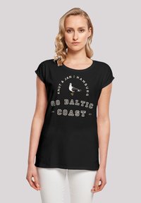 Black cotton t-shirt with a round neckline. Features white text "GO BALTIC COAST" and a graphic of a seagull. Relaxed fit with rolled sleeves.
