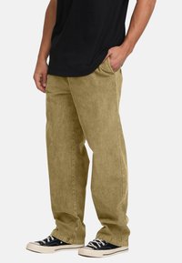Khaki corduroy pants with a straight-leg cut, featuring side pockets and a soft texture, paired with black canvas sneakers.