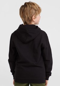 Svart hoodie med mjuk textur, ribbade muddar och en kenguruficka, sedd från baksidan på ett barn.