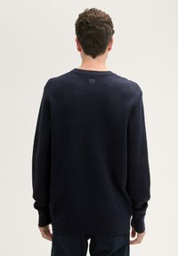 Maglione blu navy con lavorazione a maglia testurizzata, scollatura a girocollo e polsini a costine. Presenta un'etichetta piccola sul retro del collo. Vestibilità comoda.