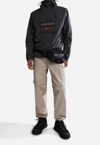 Sort vindjakke med en frontlomme og logo, beige cargo bukser med lynlåse og sorte sneakers. Har justerbare manchetter og en bæltetaske.