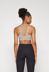 Gray sports bra with a crossed back strap design and textured surface; paired with black high-waisted leggings.
