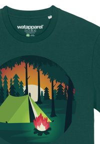Donkergroene katoen t-shirt met een circulaire afbeelding van een tent, kampvuur, bomen en een zonsondergang in oranje en gele tinten.