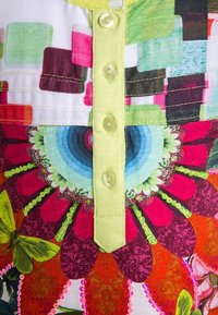 Bunt bedruckter Stoff mit Blumenmustern, der konzentrische Kreise zeigt, mit einer hellgelben Knopfleiste, verziert mit Pailletten und verschiedenen Farbtönen.