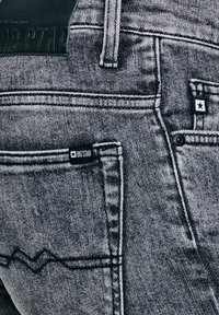 Lähivõte tuhmiks kulunud mustadest teksapükstest, millel on tagataskud, vööaas ja "BIG STAR" kaubamärgiga sildid tähelogodega.