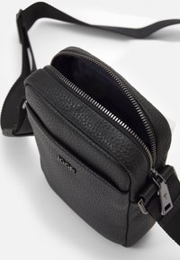 Borsa a tracolla nera in pelle con superficie testurizzata, scomparto principale con zip e tracolla regolabile intrecciata. Accentuata da un dettaglio con logo.