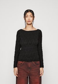 Langsleeve zwart top met een textuur golfpatroon, wijde halslijn en aansluitende silhoet, gecombineerd met donkerrode wijde jeans.
