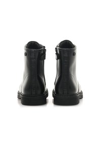 Botas negras hasta el tobillo con un acabado de cuero brillante, con una correa negra texturizada a lo largo de la parte posterior y una suela de goma.