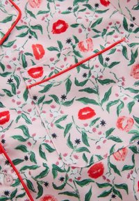 Short-sleeve fabric shirt with a pink background, featuring a floral pattern of red and green leaves, accented with red piping along the pocket.