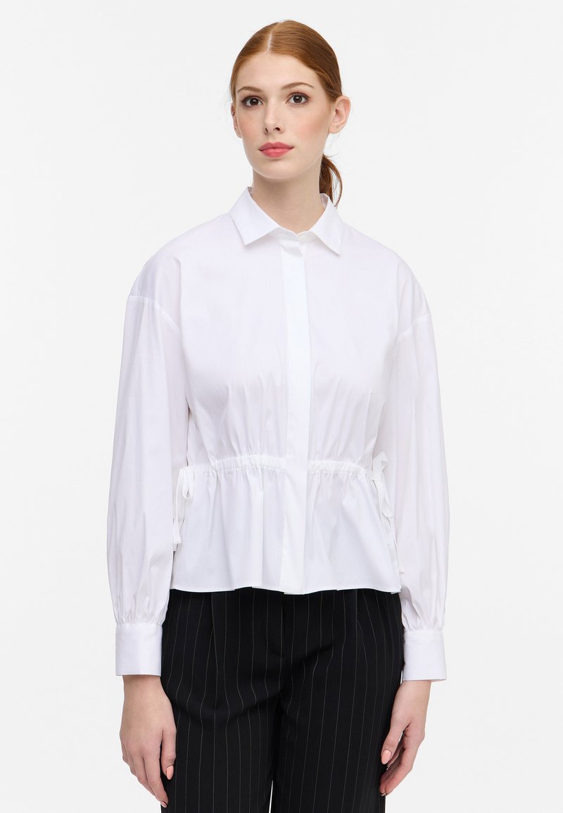 Camicia bianca con bottoni, vita arricciata, maniche lunghe e polsini. Tessuto leggero e morbido con colletto classico.