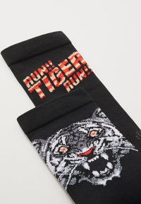 Crne pamučne čarape s grafikom tigra s crvenim očima i zubima. Gornji dio prikazuje tekst "TRČI! TIGRE, TRČI!" u podebljanom tekstu.
