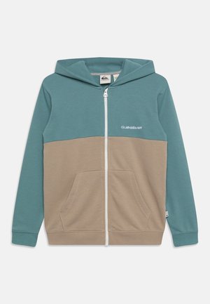 Kapuzensweatshirt mit Reißverschluss in Teal und Beige. Verfügt über eine Vordertasche, kontrastierende Einsätze und ein weißes Logo auf der Brust. Weicher Stoff.
