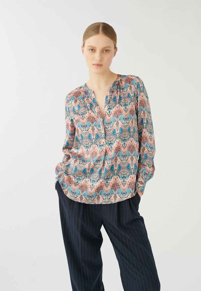 Blusa a fantasia in morbido tessuto, con un design floreale e geometrico colorato in tonalità di rosa, blu e crema; scollo a V e maniche lunghe.
