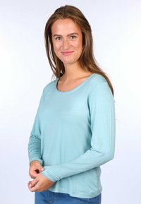 Helles blaues Langarmshirt aus weichem Stoff mit einem runden Ausschnitt und zarten gewellten Rändern an den Ärmeln. Lockere Passform.