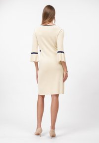 Abito beige fino al ginocchio con maniche a campana, caratterizzato da strisce blu navy sui polsini. Realizzato in un tessuto a coste. Design semplice e aderente.