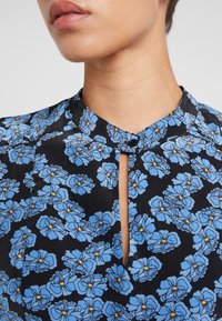 Paitsi, joka on mustalla taustalla sinisiä kukkakuoseja ja keltaisia yksityiskohtia, kauluksessa on pieni avainreikät yksityiskohta, sileää kangasta.