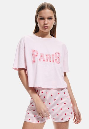 Roze cropped t-shirt met "PARIS" in hartvormige letters, gecombineerd met roze gestreepte shorts met kleine rode hartjes. Katoenen stof.