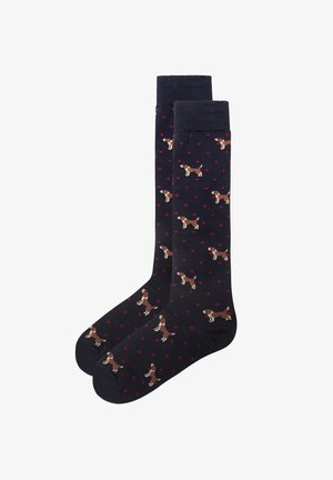 Chaussettes montantes en bleu marine foncé avec des pois rouges et un motif répété de chiens bruns dans des poses ludiques. Fabriquées en matériau doux et extensible.