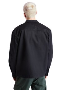 Černá koženka vyrobená z odolné tkaniny. Má límec, knoflíkové manžety a volný střih. Bez viditelných vzorů nebo rozlišujících akcentů.