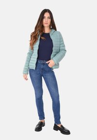 Giacca puffer blu chiaro, con cerniera, con cuciture orizzontali; top blu navy; jeans slim blu; mocassini neri con borchie.