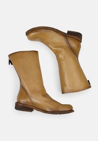Stivali ankle in pelle color cuoio con finitura liscia, punte arrotondate, cuciture minime e tacco leggero. Presentano una cerniera sul retro per la chiusura.