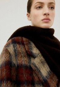 Abrigo de mezcla de lana con un patrón de cuadros en marrón, azul y óxido; cuello alto y textura suave; detalle visible en la solapa.