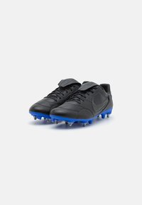 Botas de fútbol de cuero negro con acentos azules, que presentan un cierre con cordones en la parte delantera y una correa de velcro. Diseñadas con tacos moldeados para mayor tracción.