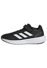 Chaussure de sport noire avec une semelle blanche et trois bandes blanches sur le côté, dotée de lacets et d'une sangle Velcro noire sur le dessus.