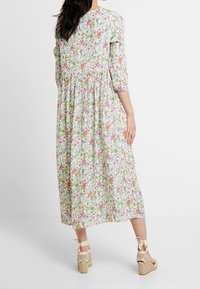 Robe midi fleurie avec une taille cintrée, des manches trois-quarts et un fond clair. Présente des motifs de fleurs colorées et un design fluide.