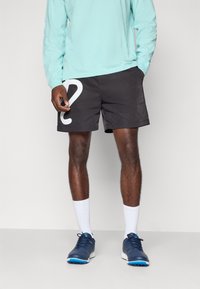 Black swim shorts with white question mark graphic, paired with a light blue long-sleeve shirt and navy athletic shoes. Cotton-and-polyester blend.