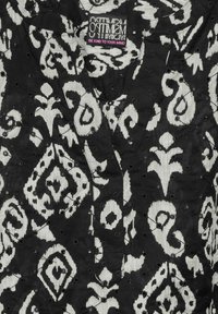 Tessuto a righe in bianco e nero con disegni a spirale, arricchito da dettagli ricamati testurizzati. L'etichetta recita "Ottimismo: Sii gentile con la tua mente."