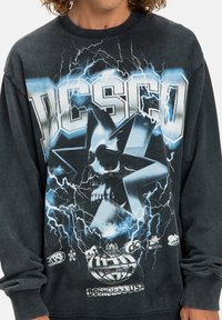 Sudadera gris oscuro con un estampado gráfico de una calavera dentro de una estrella, motivos de rayos y logotipos de la marca en la parte inferior. Puños acanalados.