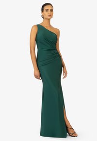 Grünes Ein-Schulter-Kleid aus glattem Stoff, mit Rüschen-Details, einem seitlichen Schlitz und einem bodenlangen Design. Strappy schwarze Absätze.