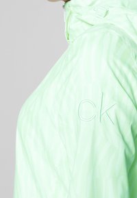 Light green jacket with a subtle striped pattern, featuring an embroidered "ck" logo on the shoulder and a high collar design.