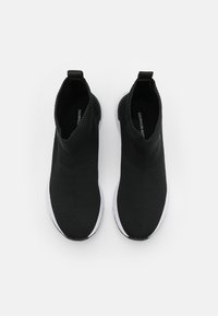 Czarne dzianinowe sneakersy z wysoką konstrukcją wokół kostki, z teksturowaną powierzchnią i białą gumową podeszwą. Minimalne oznaczenia marki widoczne wewnątrz.