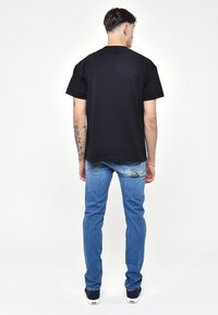 Musta puuvillapaita, pyöre ä kaula-aukko, lyhyet hihat; yhdistettynä sinisiin farkkuihin, joissa on kolmiomainen taskuyksityiskohta ja slim fit.