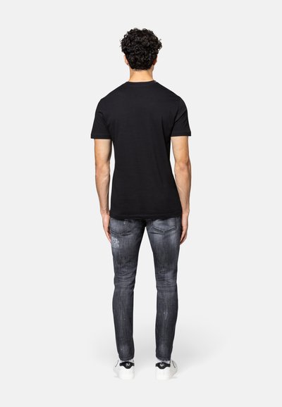 Zwarte t-shirt met korte mouwen, gecombineerd met vervaagde grijze jeans. Het shirt heeft een standaard snit; de jeans hebben een verouderd patroon en achterzakken.