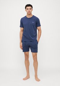 Mörkblå bomulls t-shirt och shorts-set, med rund halsringning och minimal logotyp. Mjuk textur, avslappnad passform, lätt design.